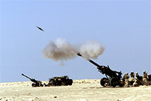 A 155 mm artillery shell is visible as it exits the barrel of an M-198 howitzer during training