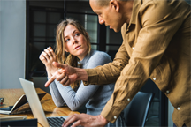 A man, standing, explaining something to a woman, seated