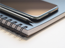 A spiral notebook, a pencil, and a mobile device